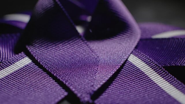 Close up of shiny purple ribbon with white stripes, shallow depth of field, detailed fabric texture, dark background