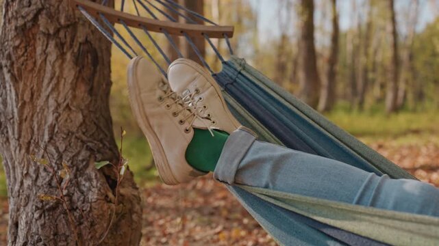 Hammock camping sunset with tan boots perched. Golden light through pine, jeans and green socks in relaxed pose, backpacker pausing at dusk, peaceful woodland scene, warm evening tones, reflective