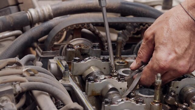 Hands adjust engine parts with care and precision. Tools rest on metal components, showing mechanic's focus. No visible emotion, but concentration is evident. Ideal for automotive repair