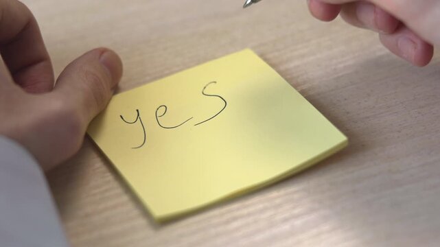 Note Taken With Neat Handwriting. Individual Diligently Writes On Sticky Pad In Quiet Office Setting. Media