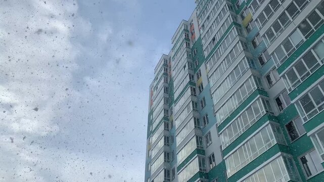 A modern residential apartment building rises into a cloudy winter sky as light snow falls softly across the urban scene