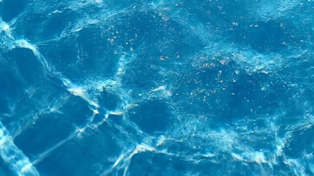 Underwater view of swimming pool water with sunlit ripples and tiling pattern, conveying refreshment and relaxation
