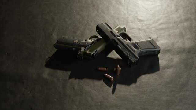 Two pistols rest on a dimly lit surface with several bullets nearby, casting deep shadows.