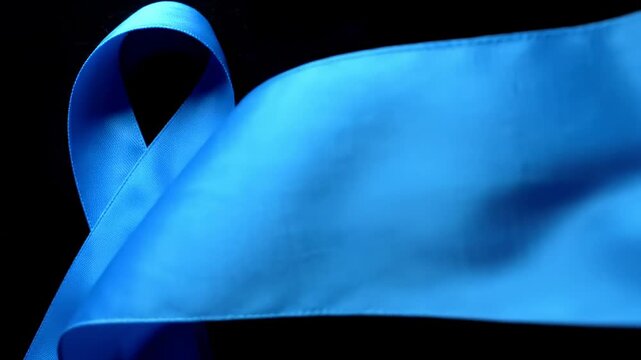 Single blue awareness ribbon curling against a dark background, symbolizing hope and support for various causes