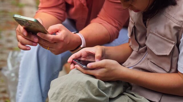 Asian mother and daughter using smartphone for digital learning and research in a park, family technology and education concept.