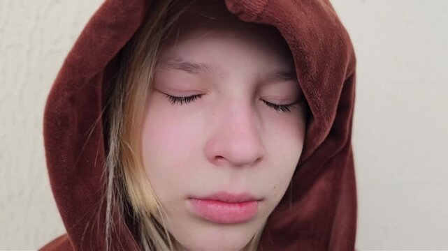 A teenage child in a hoodie looks down with tears and a serious expression. Loneliness, stress, depression, and resentment in a teenager