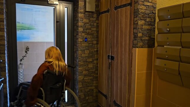 Woman in wheelchair enters a building and approaches mailboxes in a lobby area during daylight hours