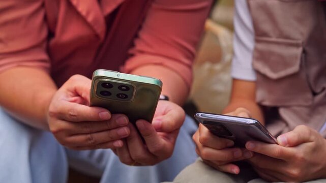 Asian mother and daughter using smartphone for digital learning and research in a park, family technology and education concept.