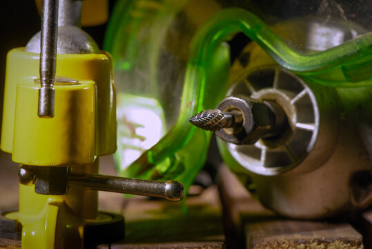 Electric straight grinder with metal burr bit fixed in clamp on wooden workbench table close up background.