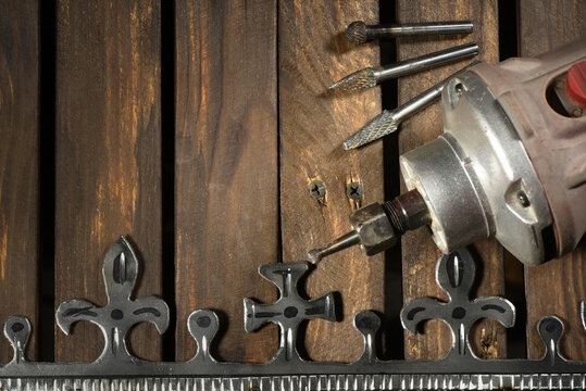 Electric straight grinder with metal milling cutter attachments for metalworking on wooden workbench table close up background.