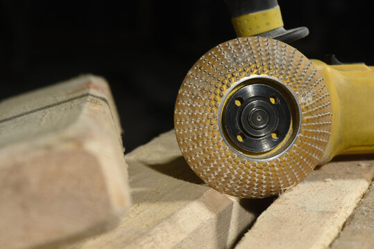 Electric angle grinder with carbide rasp disc placed on light stone blocks on workshop surface with dark close up background.