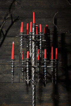 Forged wrought iron floor candelabras with twisted columns and lit red candles in dark medieval castle stronghold interior.