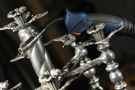 Floor standing wrought iron candelabra and electric welding torch concept during manufacturing process in blacksmith workshop.