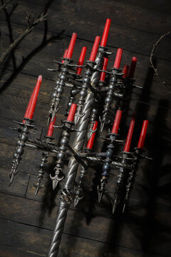 Forged wrought iron floor candelabras with twisted columns and lit red candles in dark medieval castle stronghold interior.