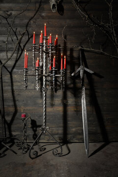 Forged wrought iron floor candelabras with twisted columns and lit red candles in dark medieval castle stronghold interior.