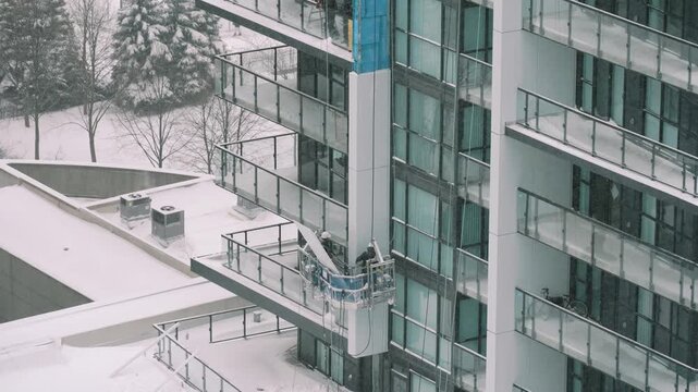 Urban worker safety. Aerial perspective of technician securing glass panels amid winter conditions on skyscraper