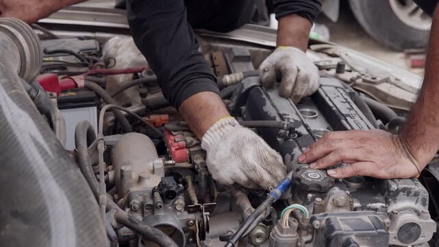 Hands work carefully on a car engine. Gloved hands adjust engine parts with precision. Mechanics focus on vehicle repairs under bright light. Ideal for auto repair, maintenance, or mechanical trades