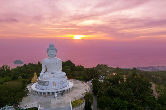 Big white marble Buddha statue sits serenely atop a lush Phuket hill top aerial view sunset purple sky