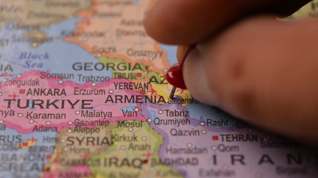 Man Marking Armenia Location with Red Pin on Paper World Map in 4K 60fps Close-Up