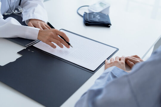 Doctor explaining treatment plan and obtaining informed consent while patient signing consent form in hospital.