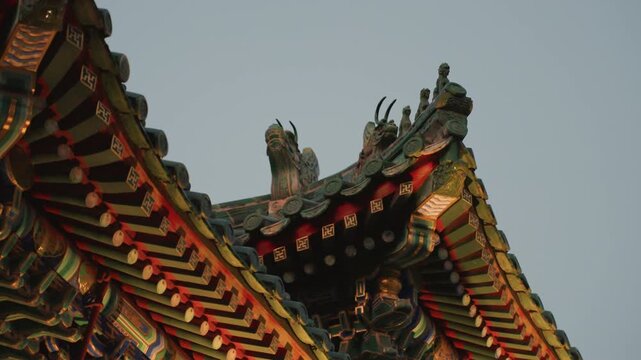 Ornate temple roof detail golden hour, intricate dragon carvings and glazed tiles catching warm light, layered eaves and painted beams, vibrant red and gold lacquer, calm twilight sky, conveys