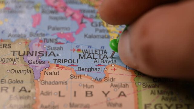 Man Marking Valletta Malta Location with Green Pin on Paper World Map in 4K 60fps Close-Up Travel Concept
