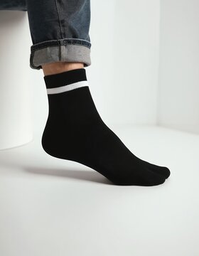Black split toe socks with white stripe detail on ankle. Casual jeans worn rolled up. Clean white studio background offers ample copy space for text or graphics.