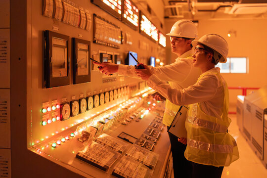 Male and female engineers working at control panel in power plant, managing clean energy systems, monitoring operations and ensuring efficiency in modern industrial technology concept