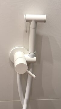 White plastic bidet hand shower sprayer mounted on clean beige square ceramic tile bathroom wall with white hose