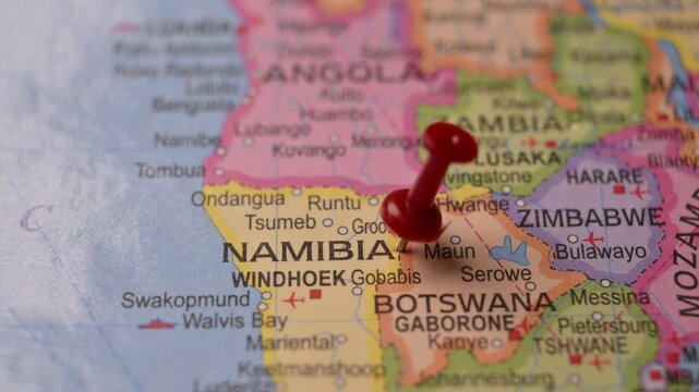 Man Marking Namibia Location with Red Pin on Paper World Map in 4K 60fps Close-Up Travel Concept