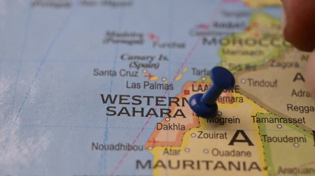 Man Marking Western Sahara Location with Blue Pin on Paper World Map in 4K 60fps Close-Up Travel Concept