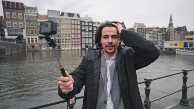 Influencer vlogging with a selfie stick on a bridge over a canal in amsterdam, netherlands