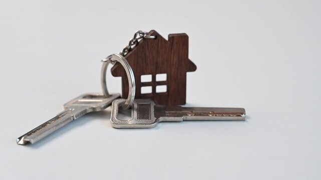Keys and a wooden house-shaped keychain spinning on a white background. 