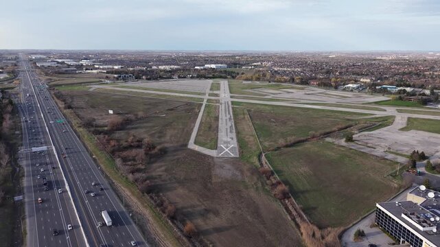 A forward-moving aerial shot descending toward the closed runways of Buttonville Airport, showing the parallel flow of traffic on Highway 404 and the surrounding urban landscape