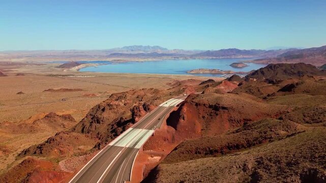 High-angle perspective of winding freeway through arid volcanic landscape near Hoover Dam at sunset.
