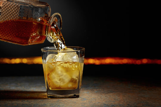 Whiskey is poured from a decanter into a glass with ice.