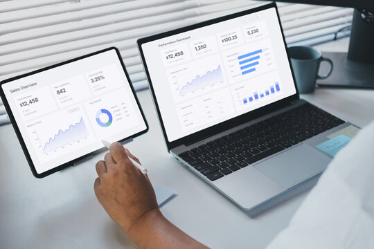 Remote work execution scene with professional analyzing saas data on laptop and tablet displaying business dashboard, performance metrics, and analytics charts, modern workspace productivity workflow