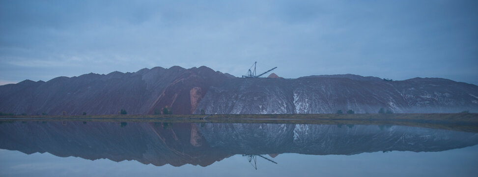 Panoramic industrial salt mounds reflected in lake water at dusk with copy space