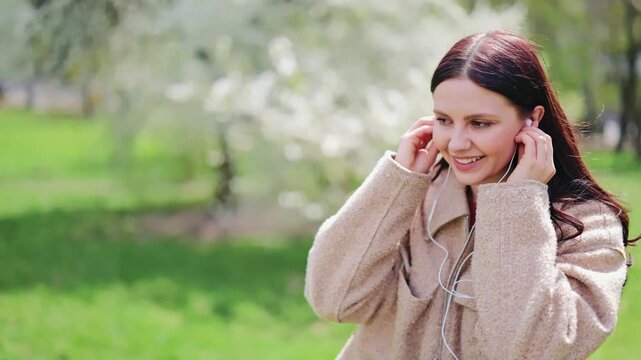 Young woman feels joy and relaxation listening to music through earbuds in vibrant spring park. Embracing peaceful moments outdoors, connected to favorite sounds. Happy expression, enjoying leisure.