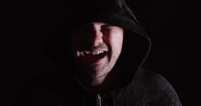 Man in a dark hoodie laughing, representing mocking behavior, bullying, and negative social interaction.