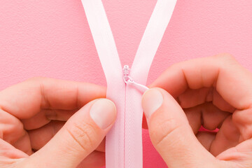 Young adult woman hand fingers holding and showing opened new pink invisible zipper for clothes on light pink table background. Pastel color. Closeup. Point of view shot. Top down view. © fotoduets