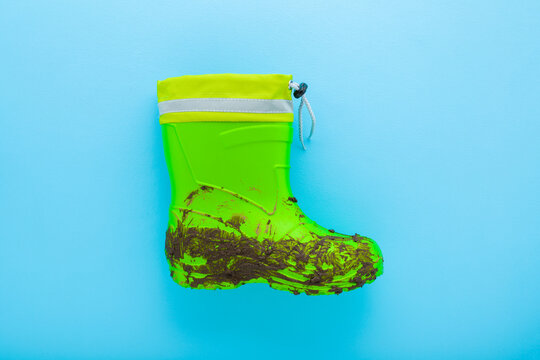 Dirty green kid rubber boot on light blue table background. Pastel color. Closeup. Flat lay. Top down view.