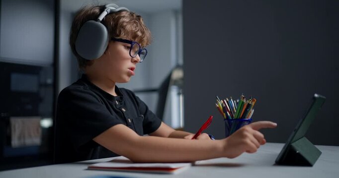 Young Boy Attentively Interacting With Tablet During Digital Classroom Session With Headphones And Supplies