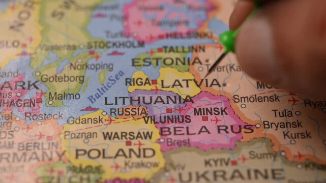 Man Marking Lithuania Location with Green Pin on Paper World Map in 4K 60fps Close-Up Travel Concept
