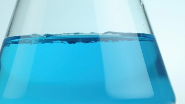 Close-up of a beaker with blue liquid, likely part of an experiment in a chemistry lab.