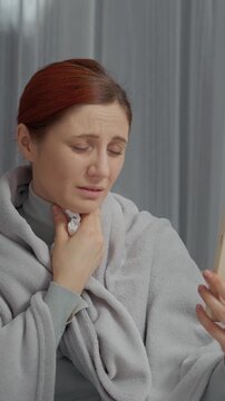 Vertical Screen: A woman sits on the couch feeling unwell while wrapped in a blanket. She is talking on the phone for medical advice about her cold symptoms and treatment options.