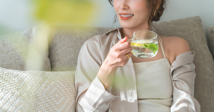 A woman sits on a sofa and drinks lemon water, detox water.