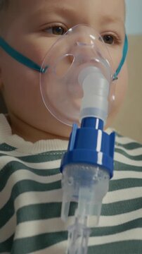 Vertical Screen: A child sits on a couch while wearing a mask to inhale saline solution. The nebulizer helps treat cough and other respiratory issues in the living room.