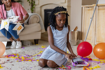 Naklejka premium African American mother and child cleaning up living room with small broom, striped dress, bunting