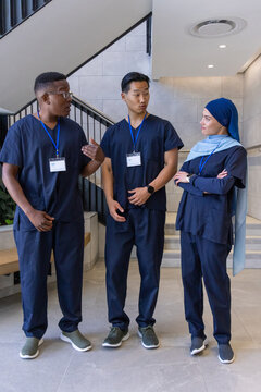 Diverse healthcare workers discussing patient case in stairwell wearing navy scrubs and lanyards